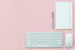 A white keyboard, mouse and notepad against a blush pink background