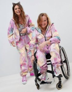 Two women, one in a wheelchair, wearing pastel, paint splattered jumpsuits from ASOS