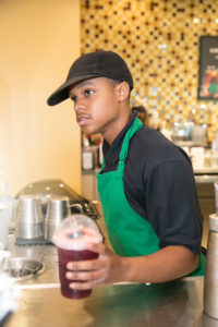 A young man serving a drink while working as a barista