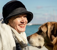 smiling woman in front of a vibrant blue body of water with her seeing eye dog