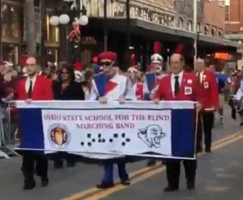members of the marching band hold up banner and play instruments during a parade