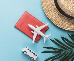 A sun hat, tropical leaf, a miniature bus and airplane, and a passport book arranged in an organized fashion with colorful accents