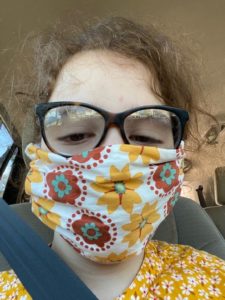 A young lady wearing glasses and a cloth face mask with flower print