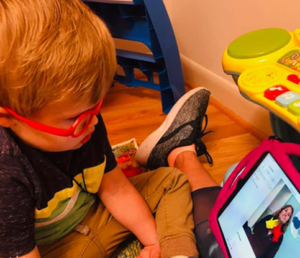 a child looks at a tablet will sitting on the floor, attending virtual therapy