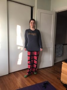 A young lady wearing a shirt with the Easterseals logo on it and pajama pants, standing in a hallway at her house