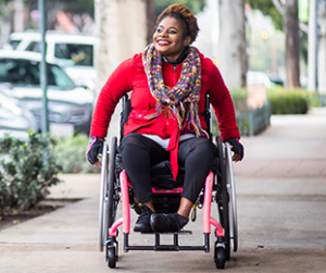 woman using a wheelchair smiling while headed down a sidewalk