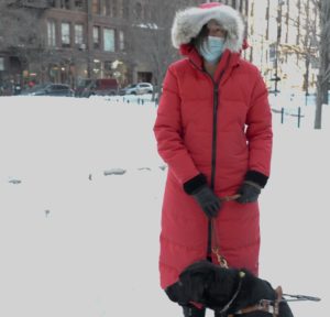 Beth and Seeing Eye Dog Luna posing in a snowy park, Beth in a long red winter coat. 