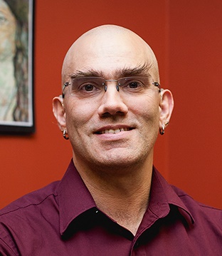 Crom Saunders. A bald man wearing a purple dress shirt, smiling