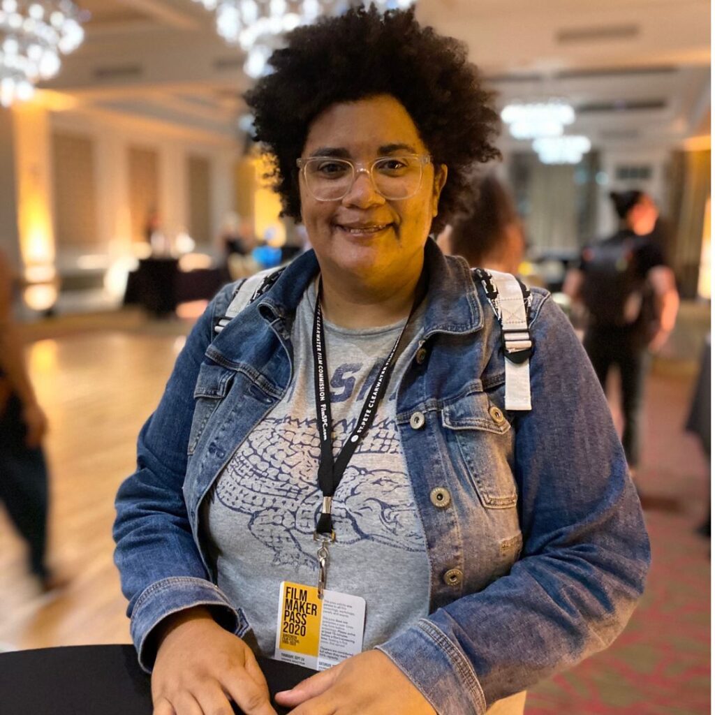 Jen at a convention with a name tag, wearing a jean jacket and smiling