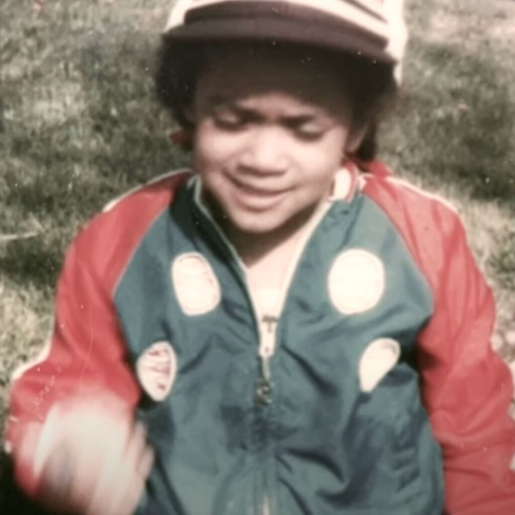 A young Jen Msumba, wearing a red a blue jacked and a baseball cap