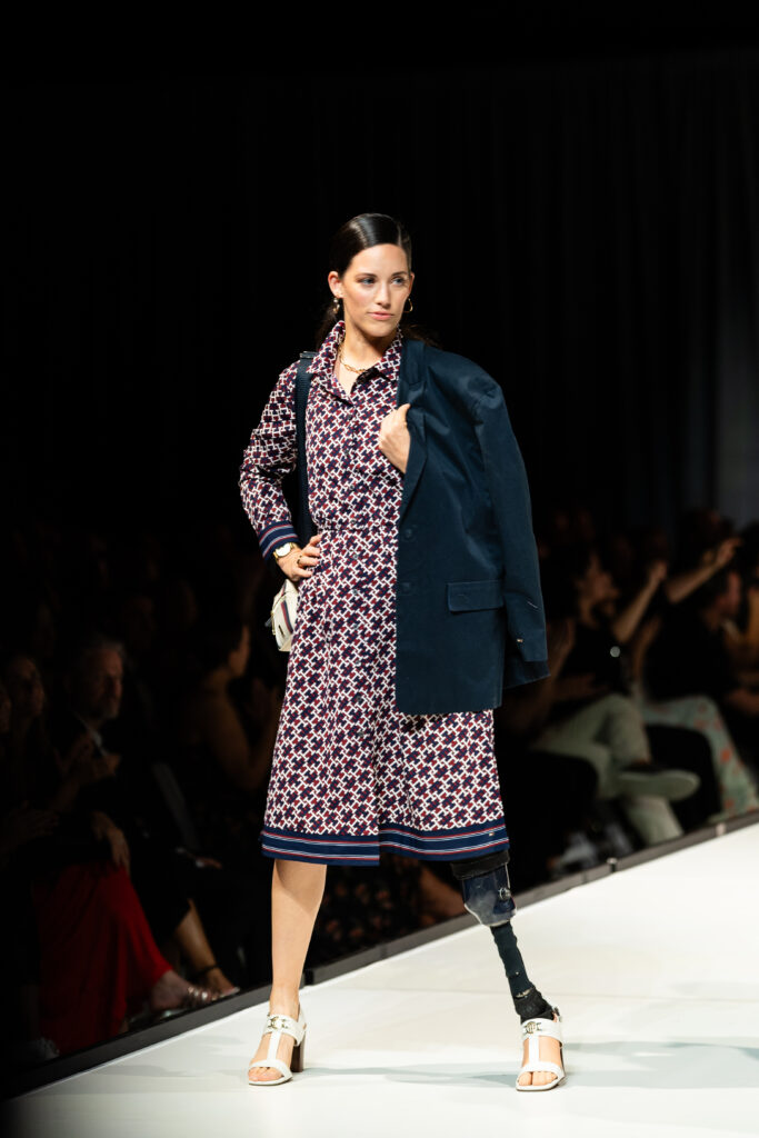 Caitlin, a leg amputee, stands on the runway in a flowered dress