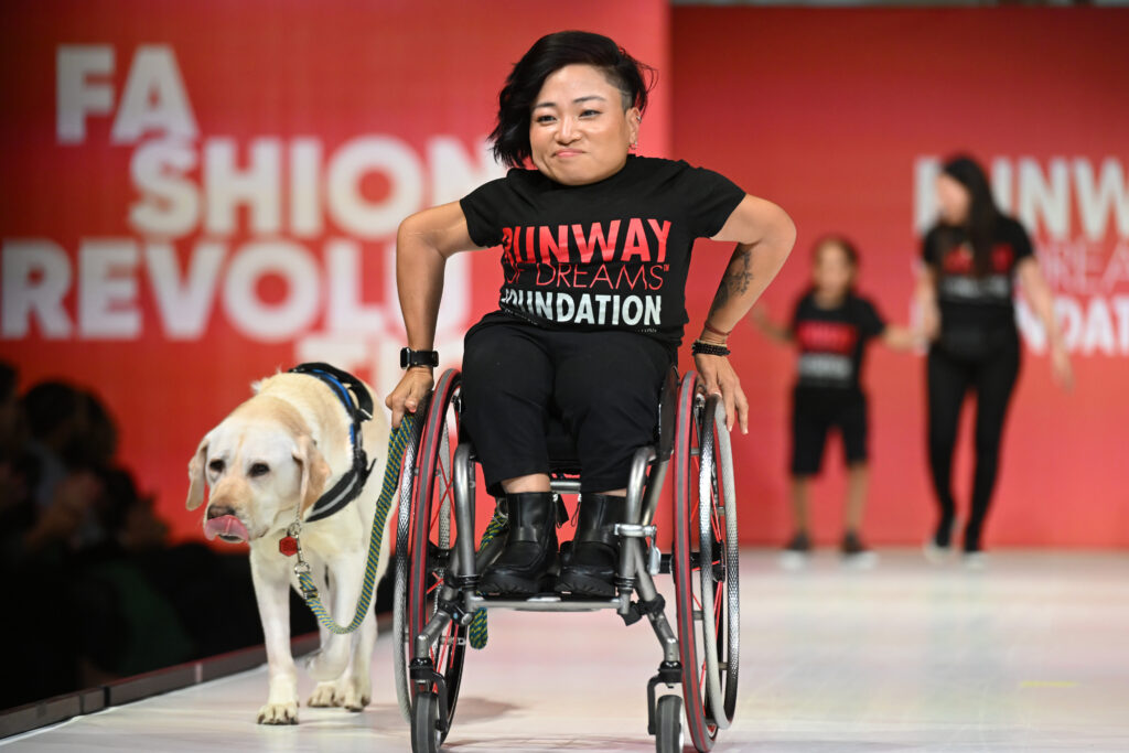 Mia using a wheelchair going down the runway with her service dog