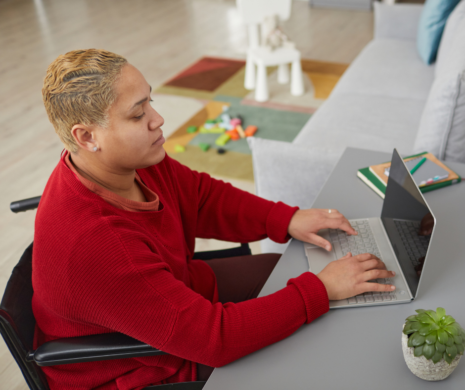 A person wearing a red sweater using a wheelchair and typing on a laptop