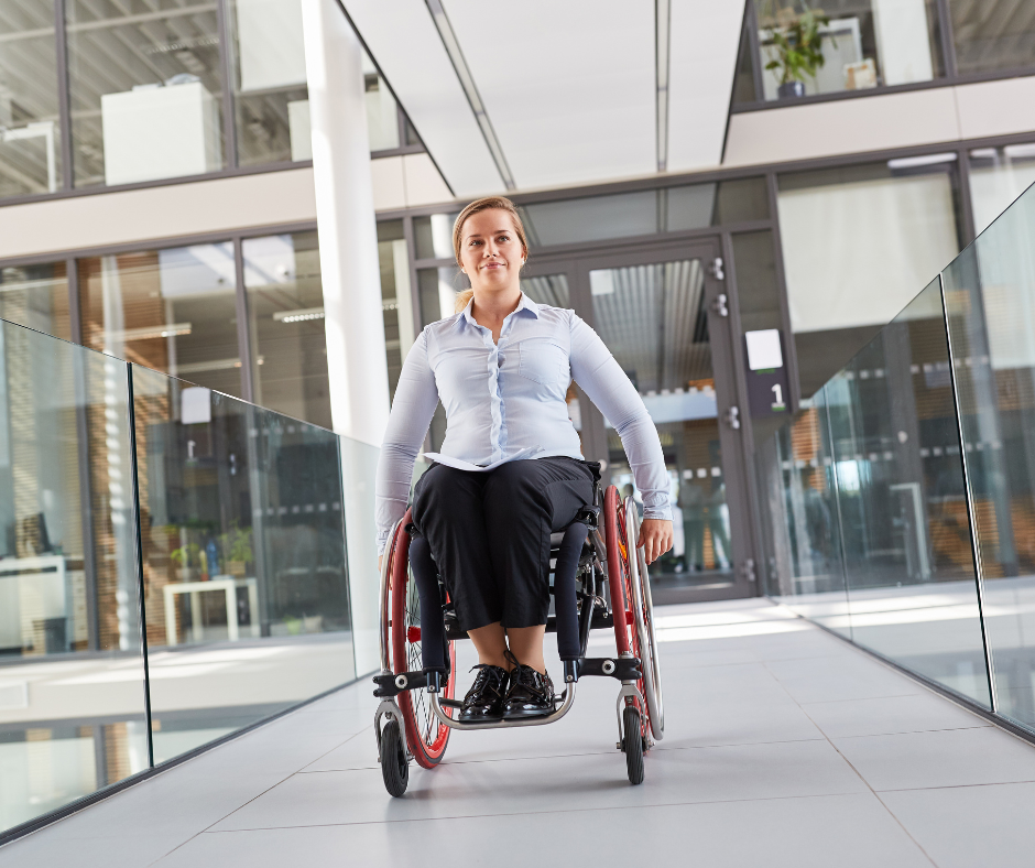 A person wearing business attire and using a wheelchair, going down a hallway in an office building