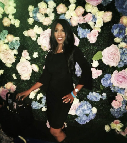 Andrea wearing a dress and standing in front of a flowered background 