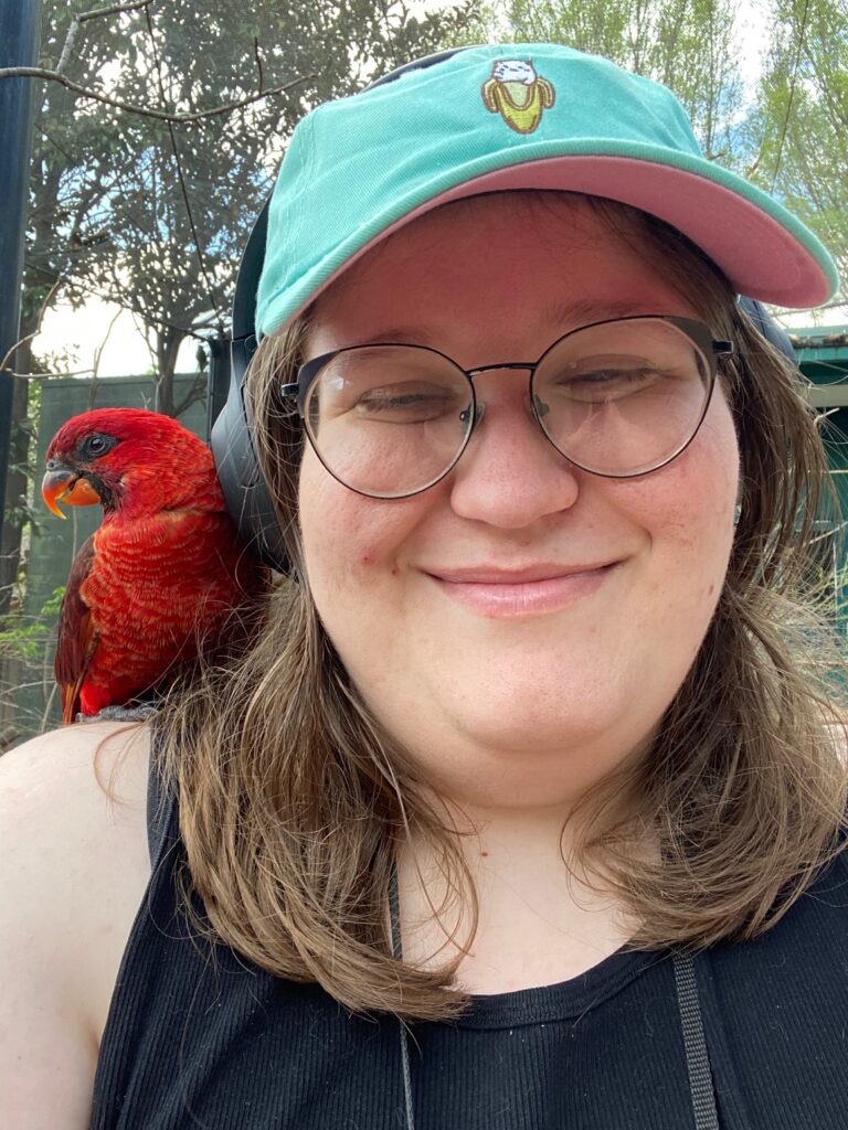 Megan with a small red bird on their shoulder