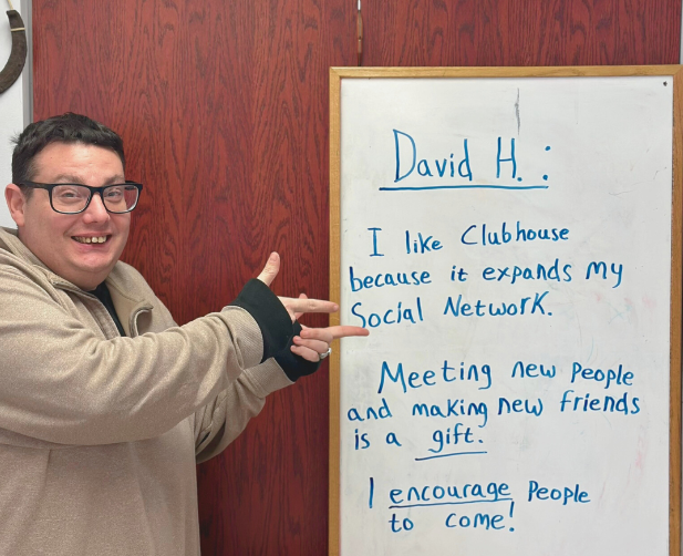 David stands in front of a whiteboard that reads "I like clubhouse because it expands my social network. Meeting new people and making new friends is a gift. I encourage people to come!