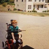 Grant as a child, driving her red wheelchair outside in the street wearing sunglasses