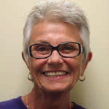 An older women with gray hair, wearing a purple shirt and black glasses 