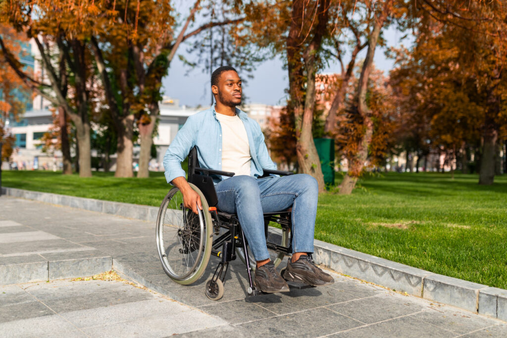 Paraplegic black man in wheelchair going down ramp on on walk at city park in autumn 