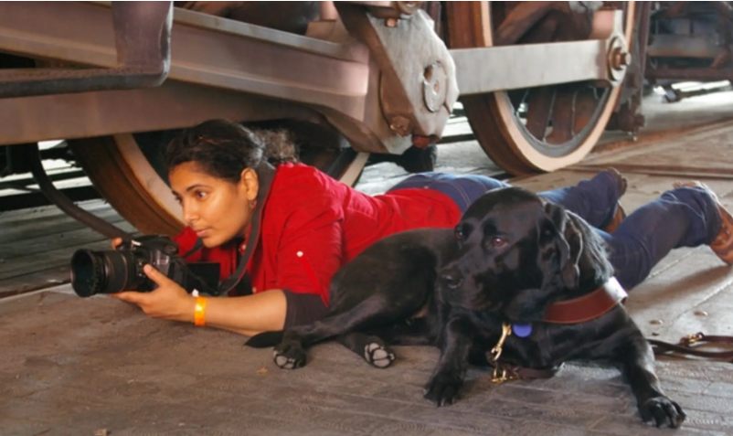 Day and her black lab lying on the ground and Day uses her camera to get an interesting shot